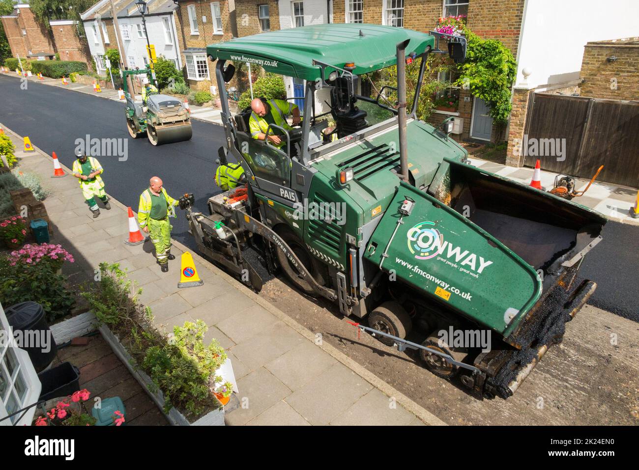 Hot tarmacadam being spread by an asphalt tarmac paver machine during resurfacing of a residential road in Twickenham, Greater London, UK. It is being resurfaced after the previous worn and potholed surface has been removed. (132) Stock Photo