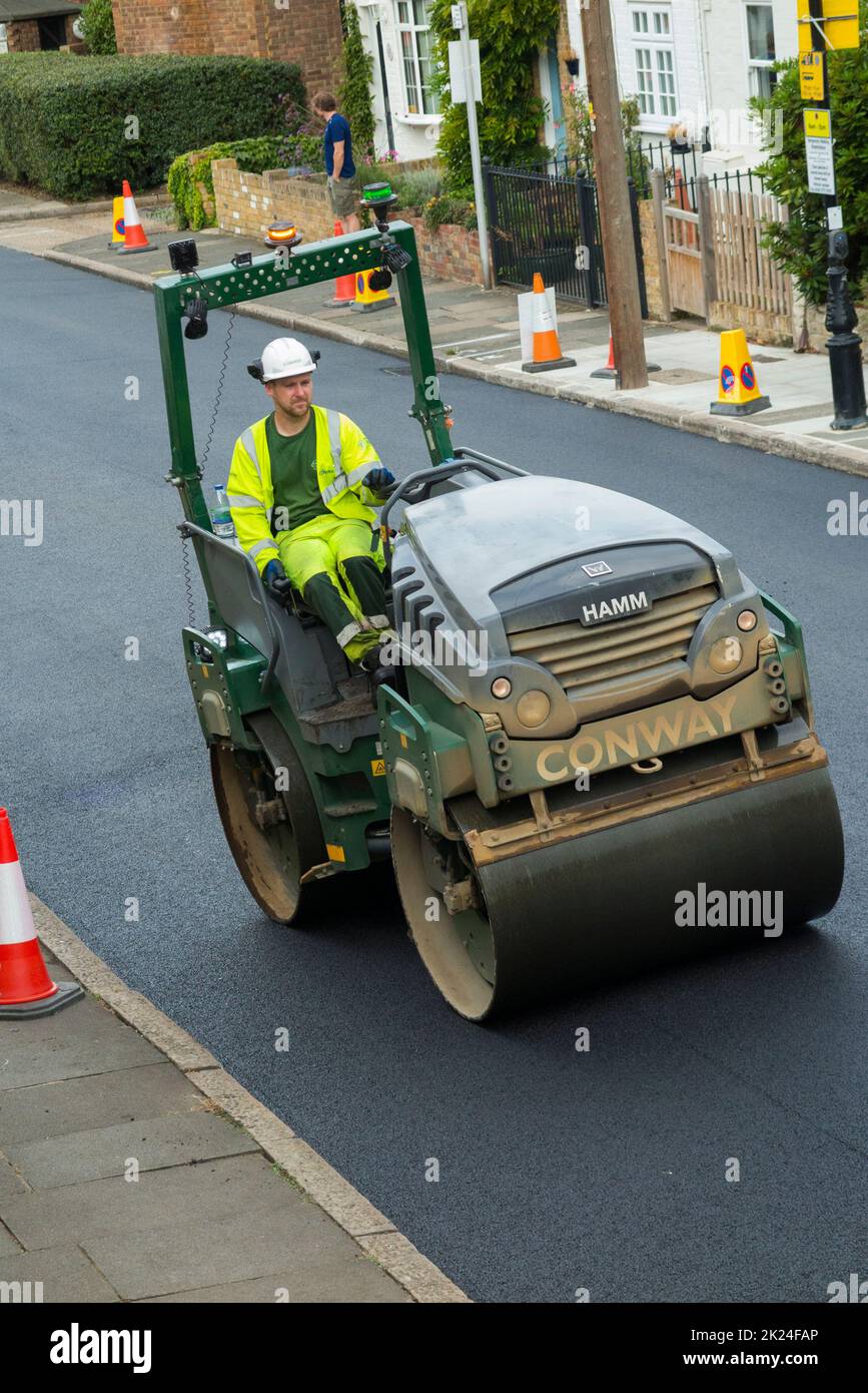 Road roller smoothing hot tarmac that has been laid while resurfacing a residential Street in Twickenham, Greater London, UK. The previous worn and potholed surface has been removed. (132) Stock Photo