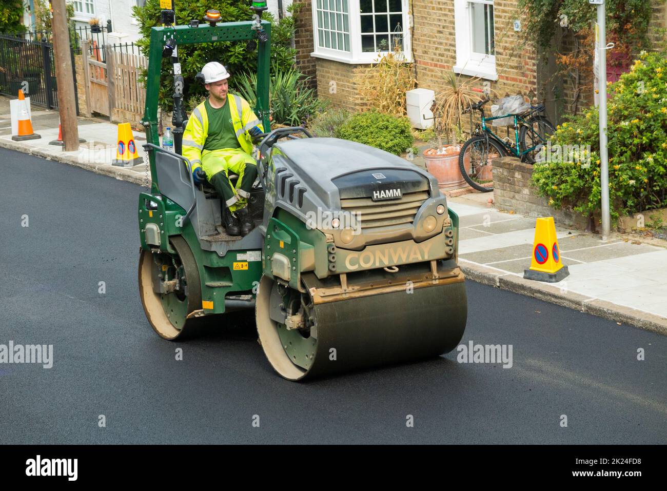 Road roller smoothing hot tarmac that has been laid while resurfacing a residential Street in Twickenham, Greater London, UK. The previous worn and potholed surface has been removed. (132) Stock Photo
