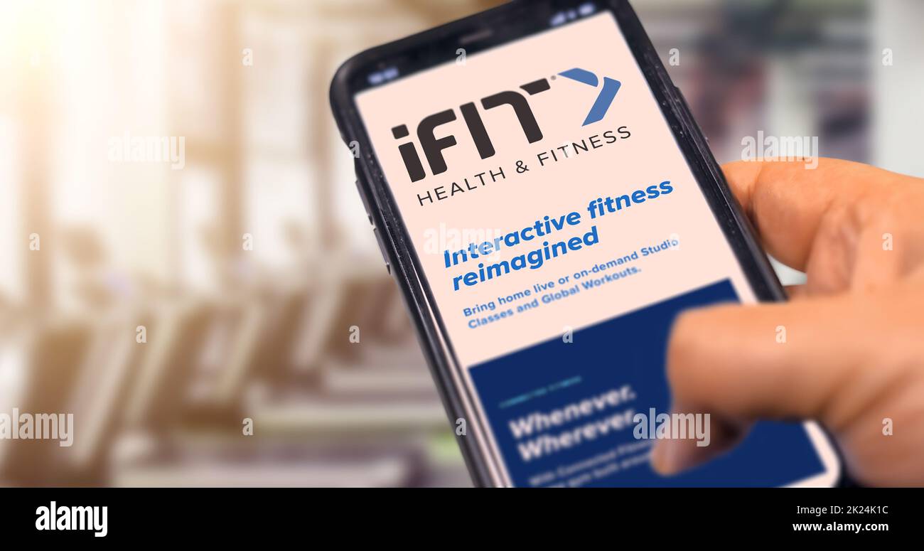 New York, USA, September 2021: hand holding a phone with the iFit mobile app on the screen with a blurred gym in the background during the day. iFIT i Stock Photo