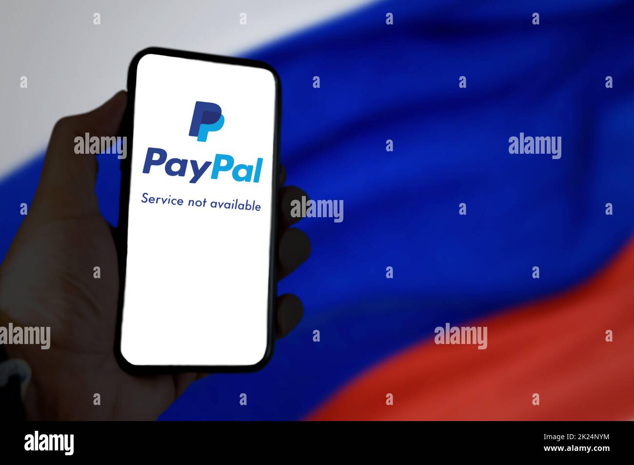 Moscow, RUS, March 2022: Hand holding a mobile phone with the Paypal app on the screen with the Russian flag blurred in the background. In March 2022 Stock Photo