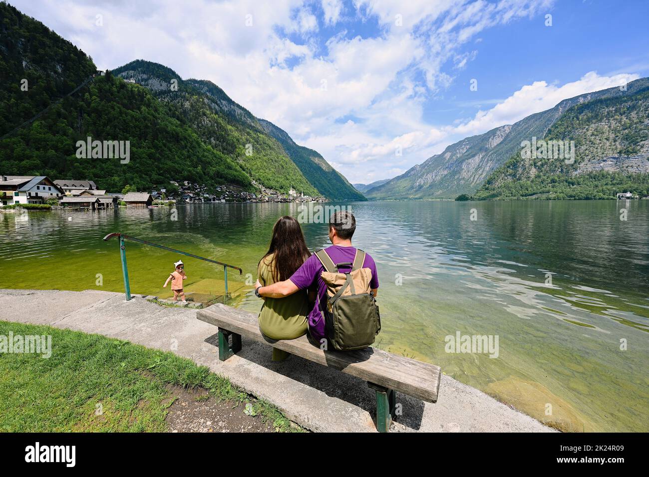 Couple with baby girl sitting on bench over Austrian alps lake in Hallstatt, Salzkammergut, Austria. Stock Photo