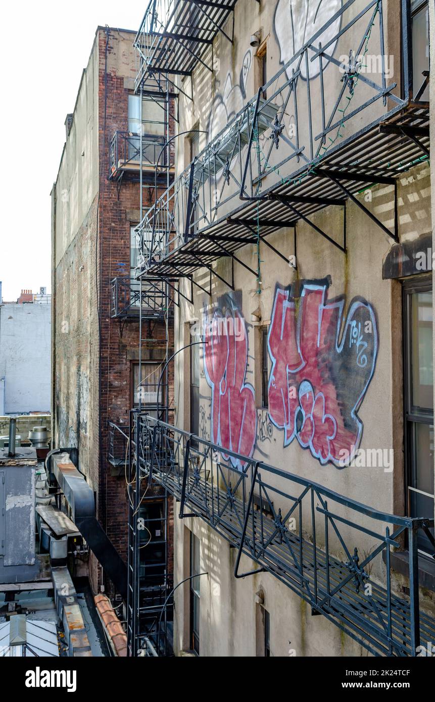 Rustic Residential Building Facade in Chelsea with Graffiti on the Wall, Emergency stairs at the Building, New York City during sunny winter day, vert Stock Photo