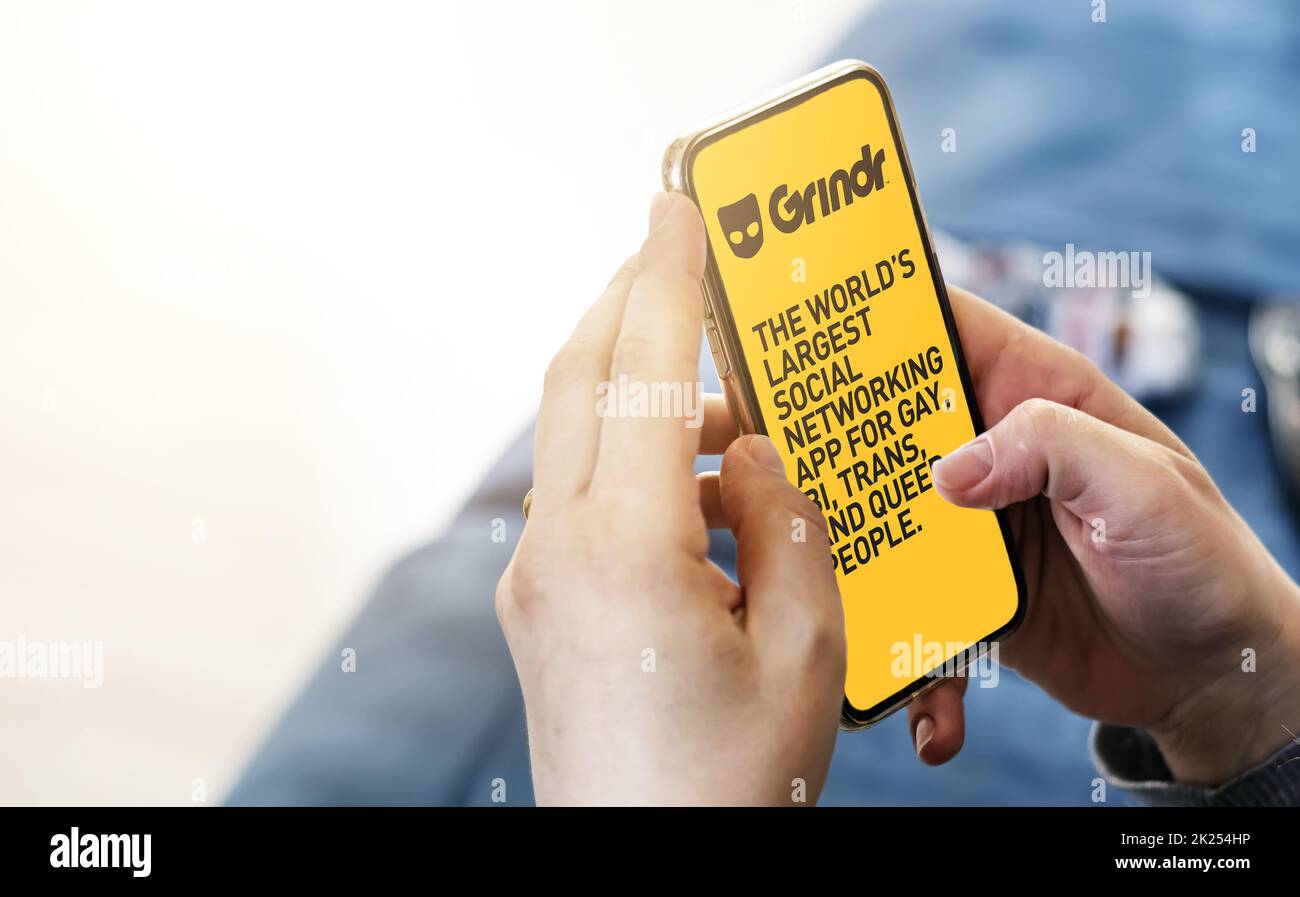 San Francisco, CA, US, May 2022: Woman holding a phone with Grindr mobile application on screen. In background the Grindr logo blurred. Grindr is dati Stock Photo