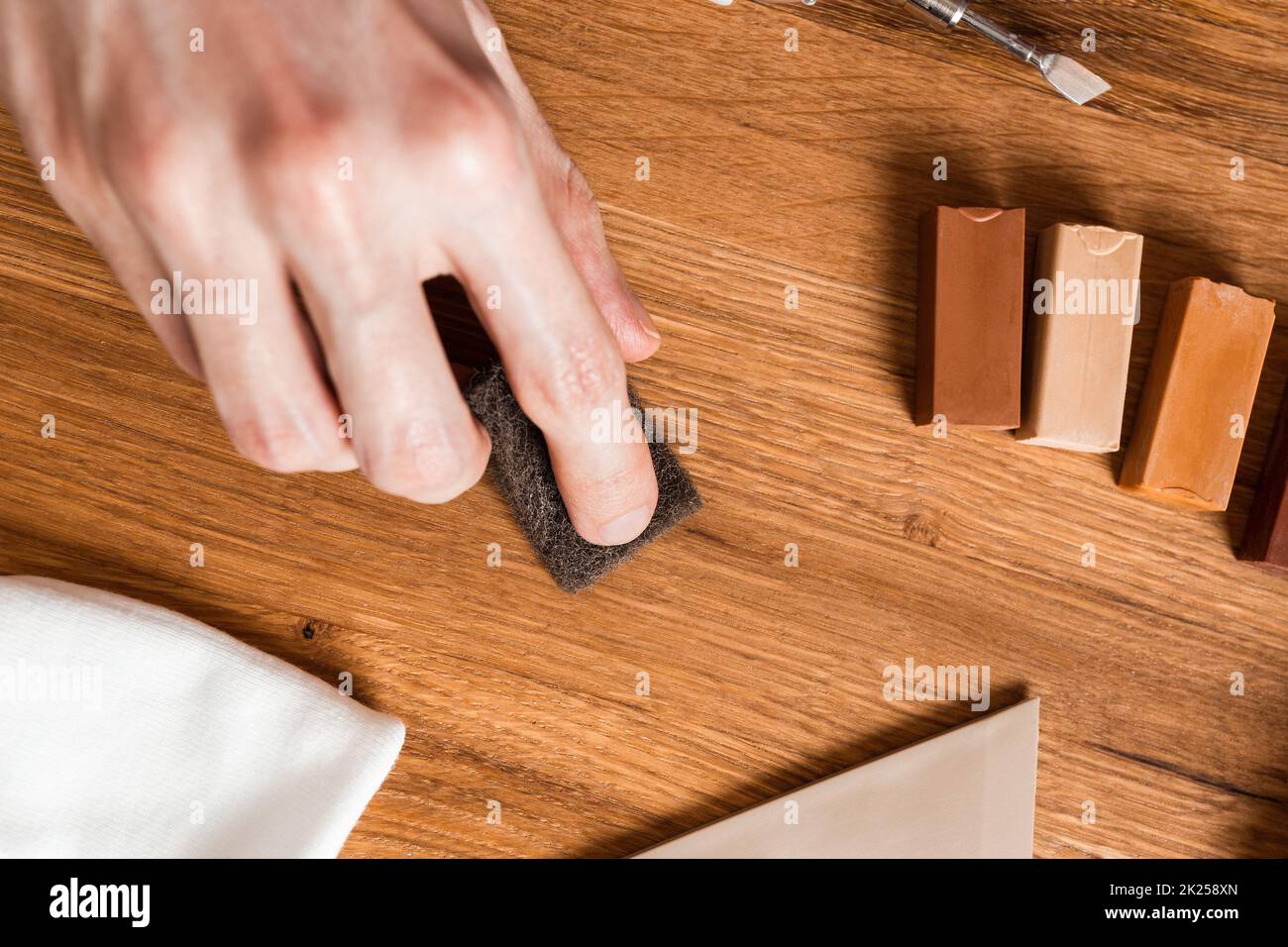 Man filling cracks, scratches, dents by wax in the wooden floor, furniture. Professional repair