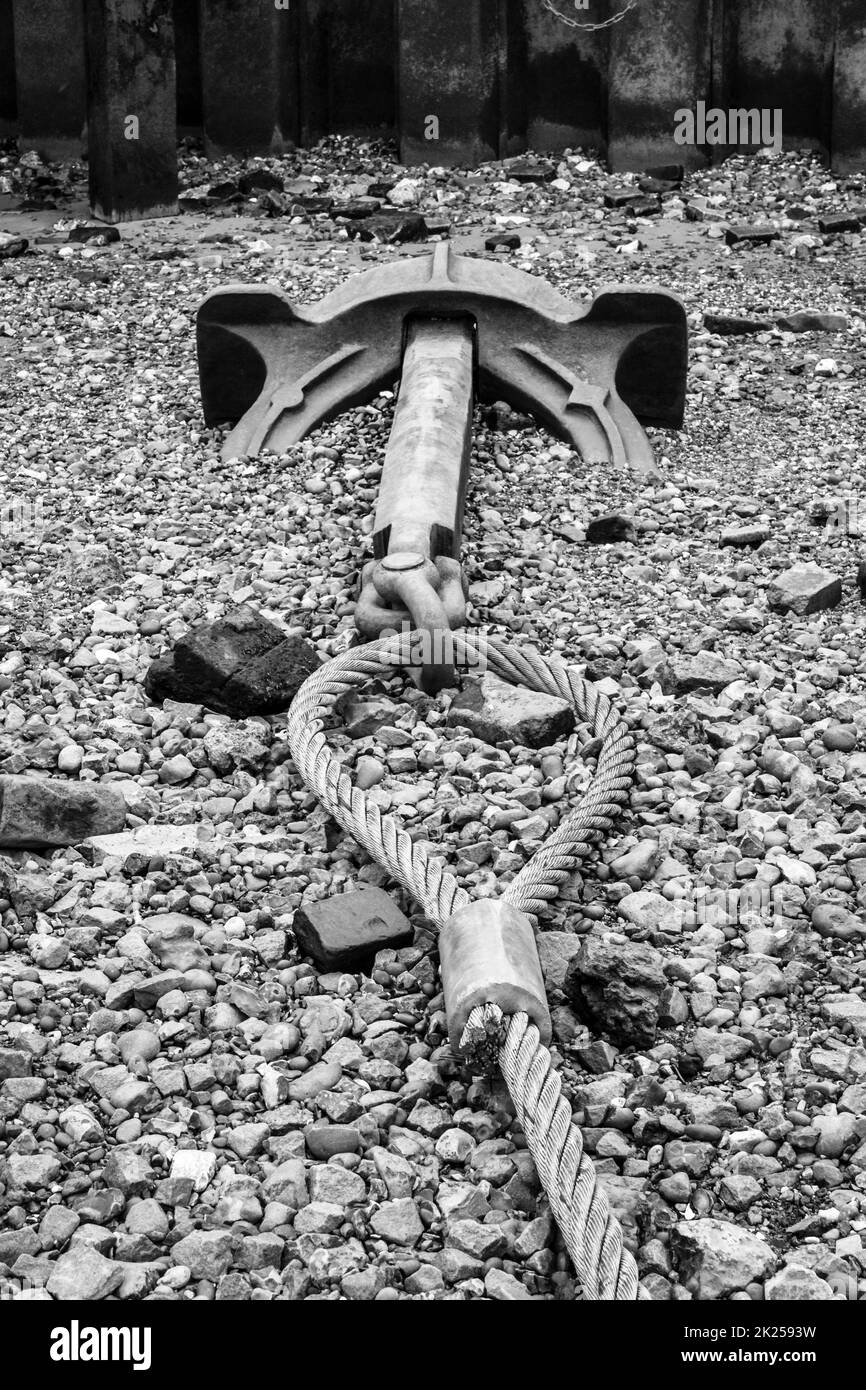 Black and white image of an anchor attached to a wire cable on the foreshore of the River Thames at low tide at Blackfriars, London, UK Stock Photo