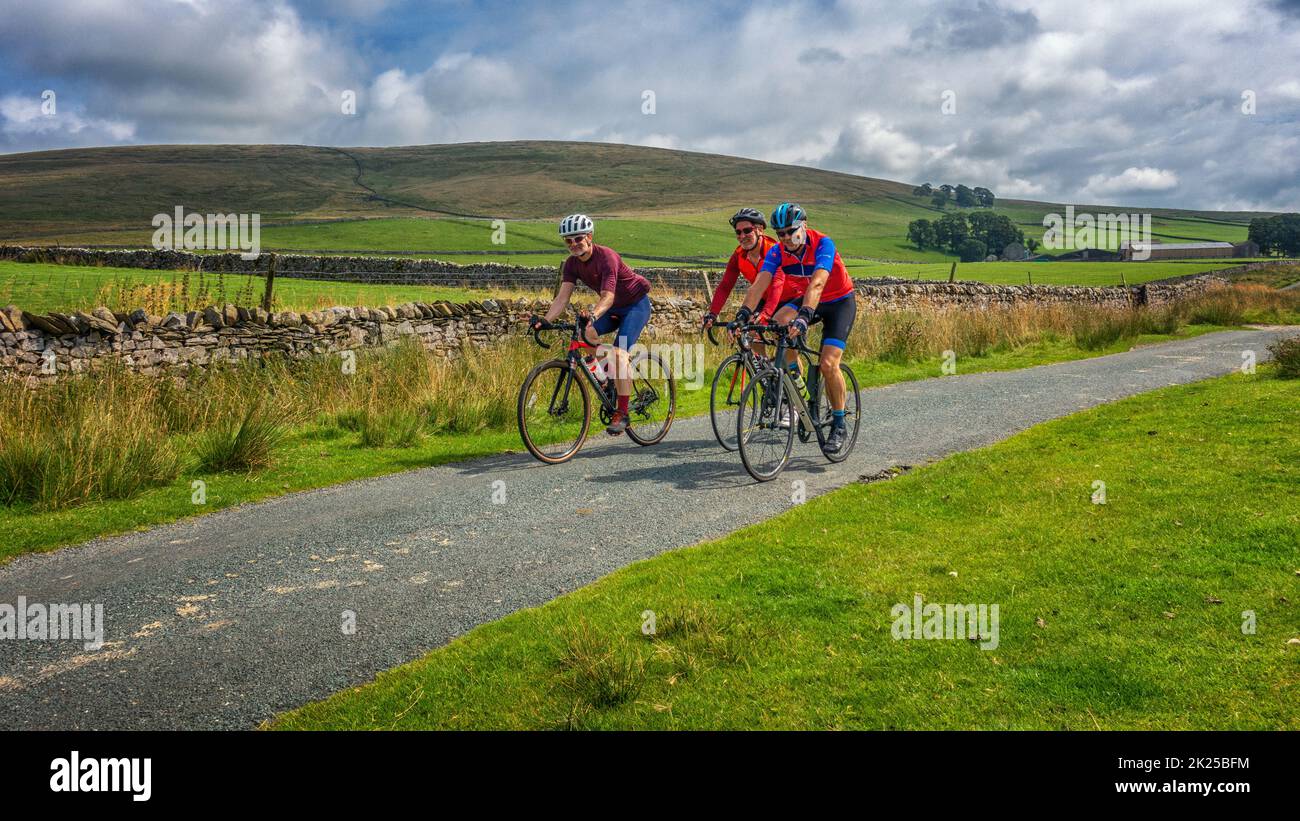 Three male cyclists socialising on bikes on a country lane over Malham Moor, Yorkshire Dales National Park, North Yorkshire, England, UK Stock Photo