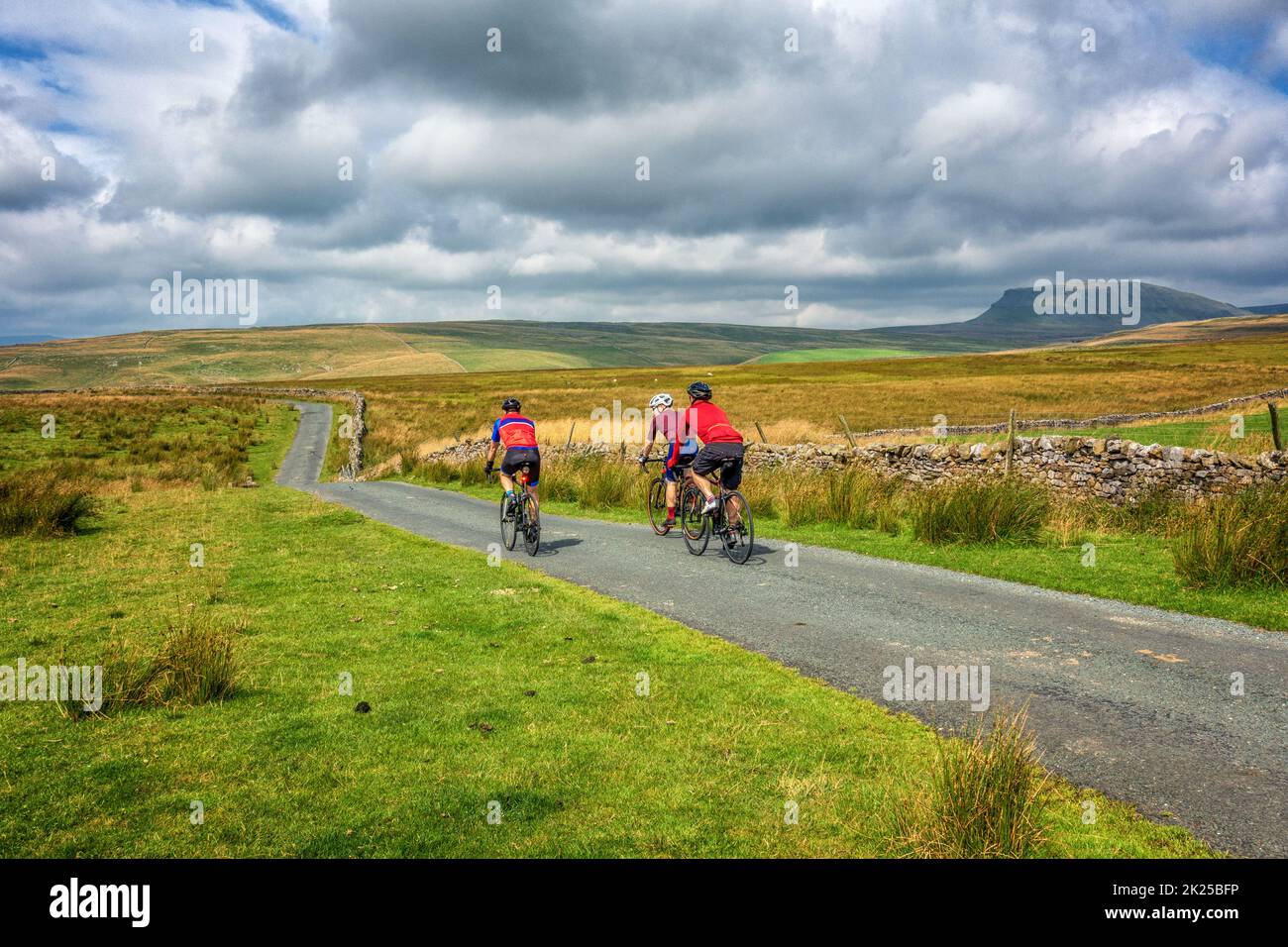 Three male cyclists socialising on bikes on a country lane over Malham Moor with views of Pen-y-ghent mountain, Yorkshire Dales National Park, North Y Stock Photo