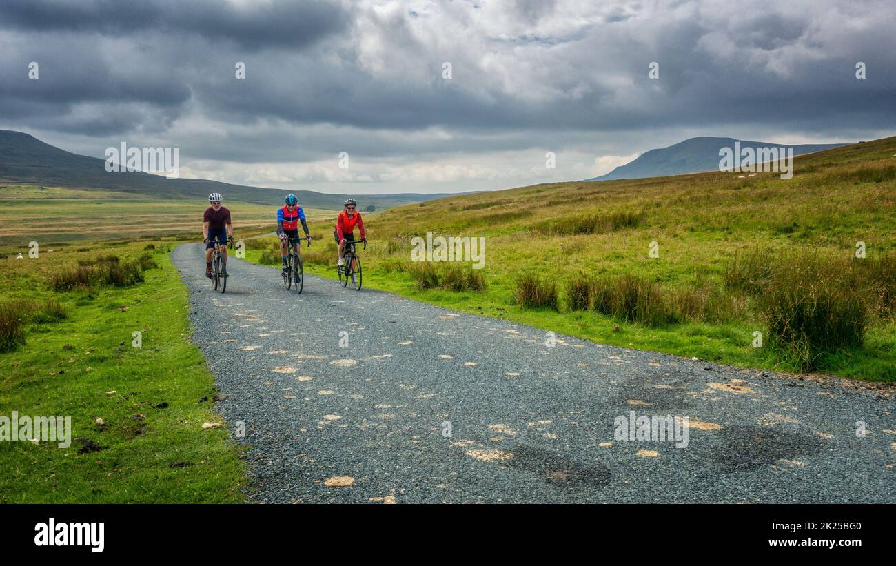 Three male cyclists socialising on bikes on a country lane near Halton Gill with views of Pen-y-ghent mountain behind, Yorkshire Dales National Park, Stock Photo