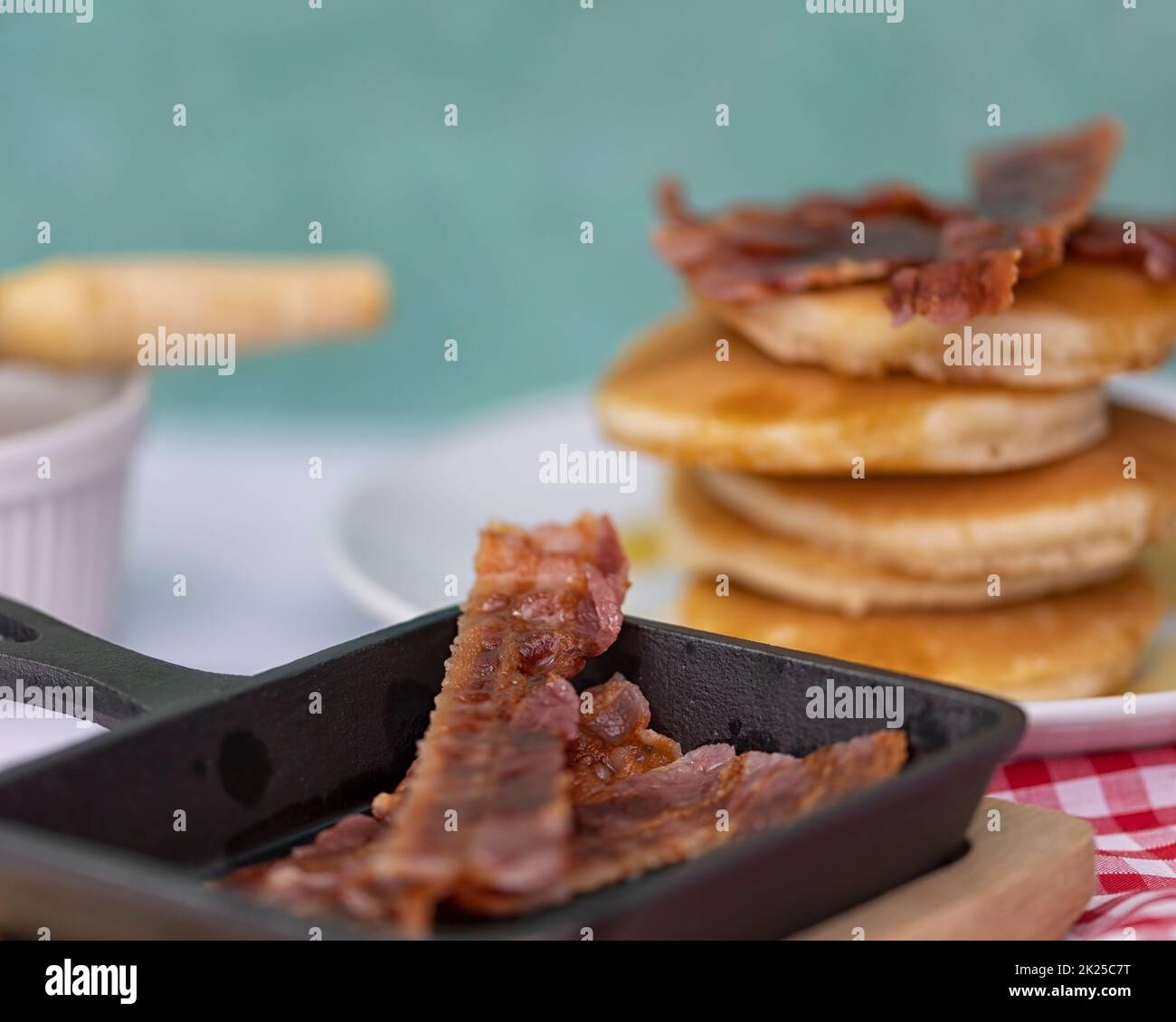 Closeup of mini cast-iron skillet with crispy bacon and pancake stack in the background Stock Photo