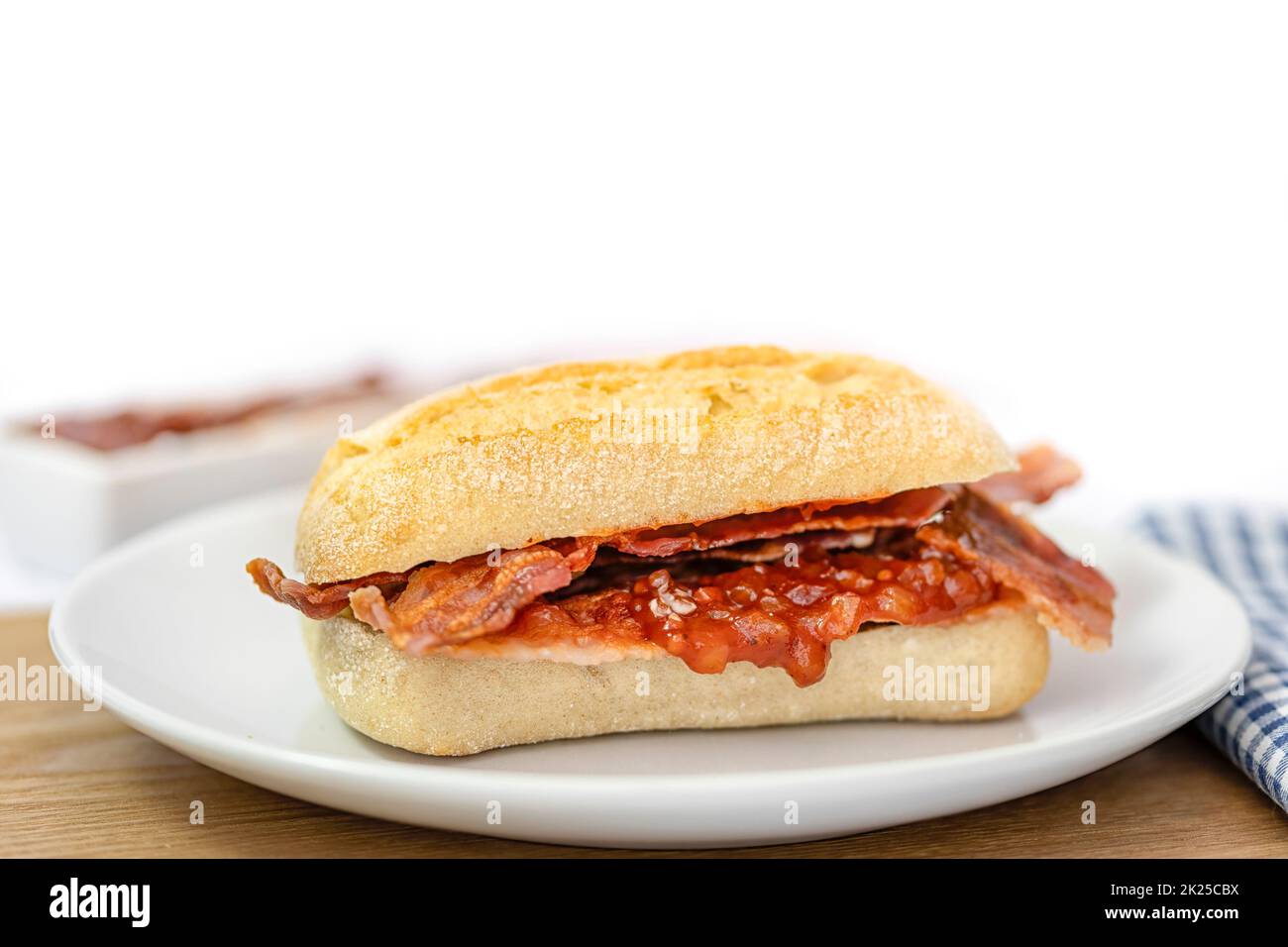 Closeup of crispy bacon in a sourdough roll on white plate Stock Photo