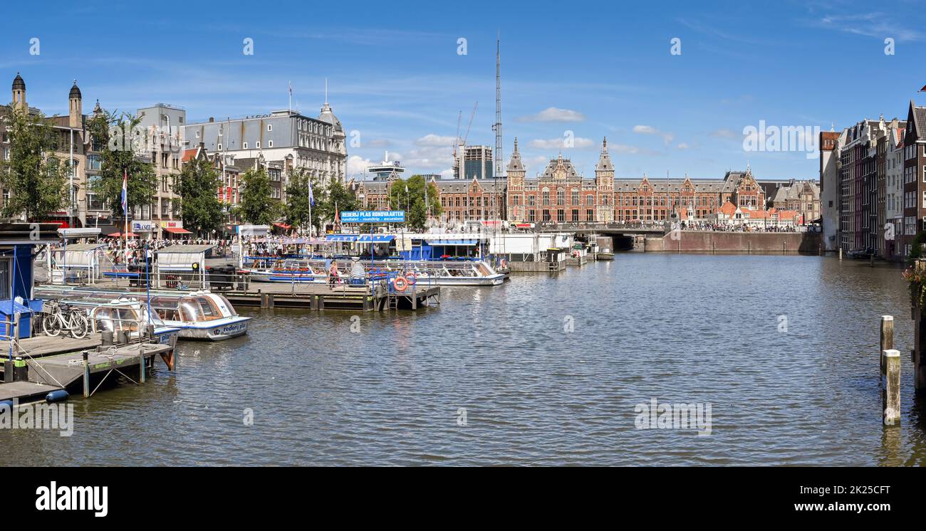 Amsterdam, Netherlands - August 2022: Tourist sightseeing canal boats moored at jettys in the city centre. In the background is the city's Centraale r Stock Photo