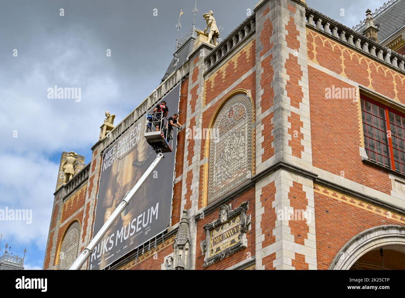 Amsterdam, Netherlands - August 2022: People standing on a cherry picker platform fixing a large banner to the outside wall of the famous Rijks Museum Stock Photo