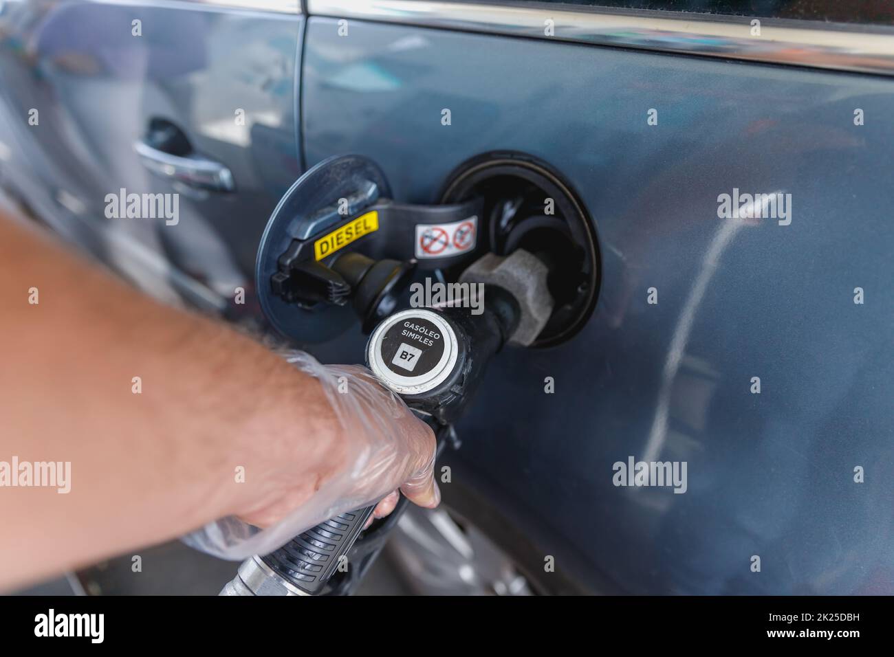 man filling the fuel tank of his car while wearing a plastic glove