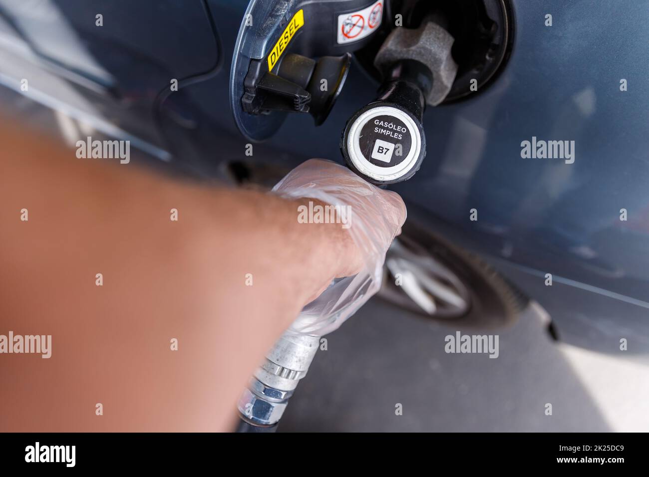 man filling the fuel tank of his car while wearing a plastic glove Stock Photo