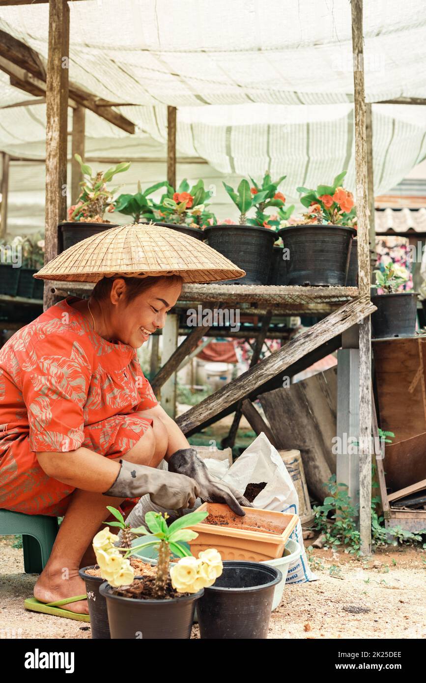 Asian female gardener is preparing soil for planting flowers into the