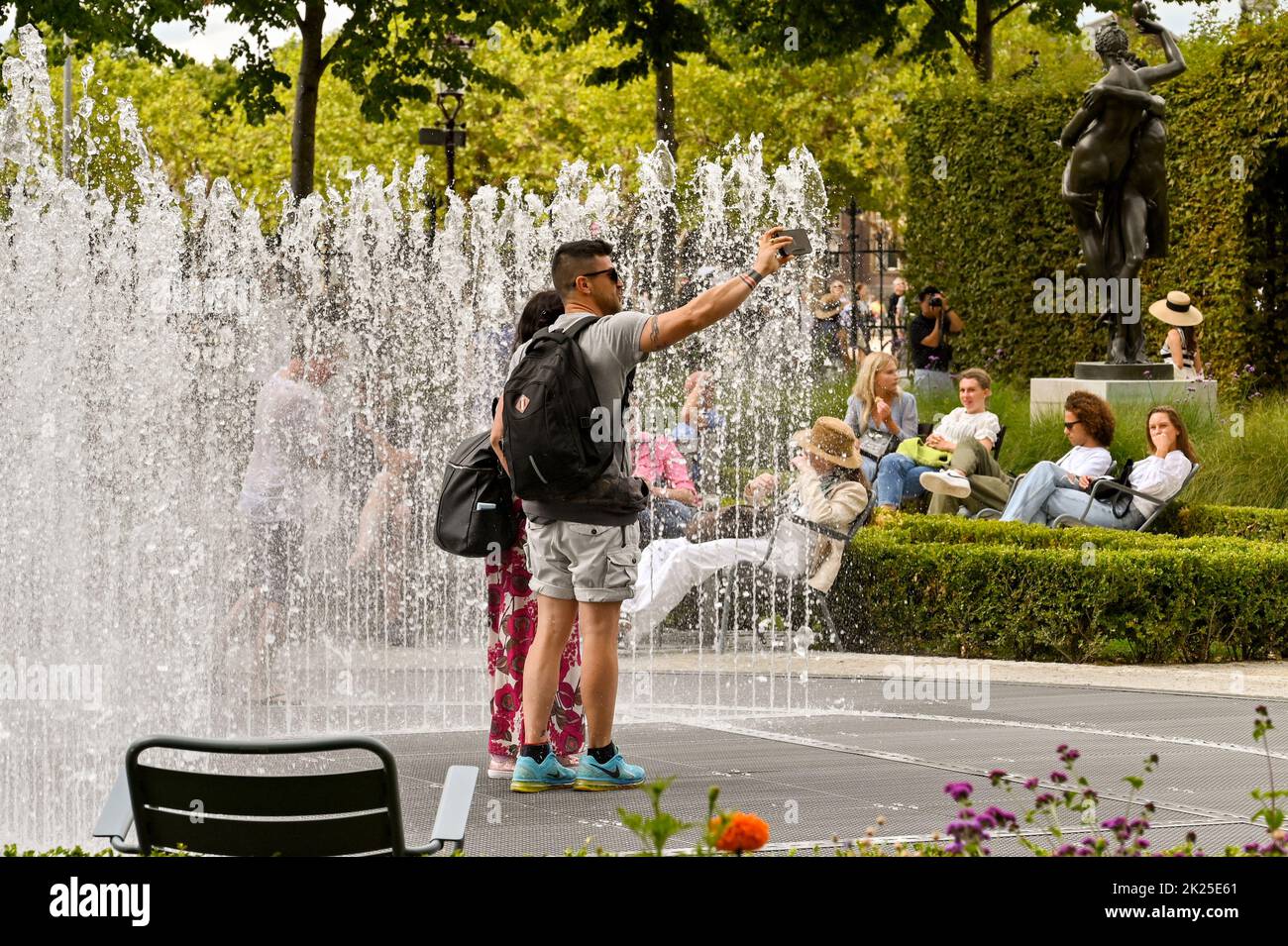 Amsterdam, Netherlands - August 2022: Two people taking a selfie while standing next to a fountain in a public garden Stock Photo