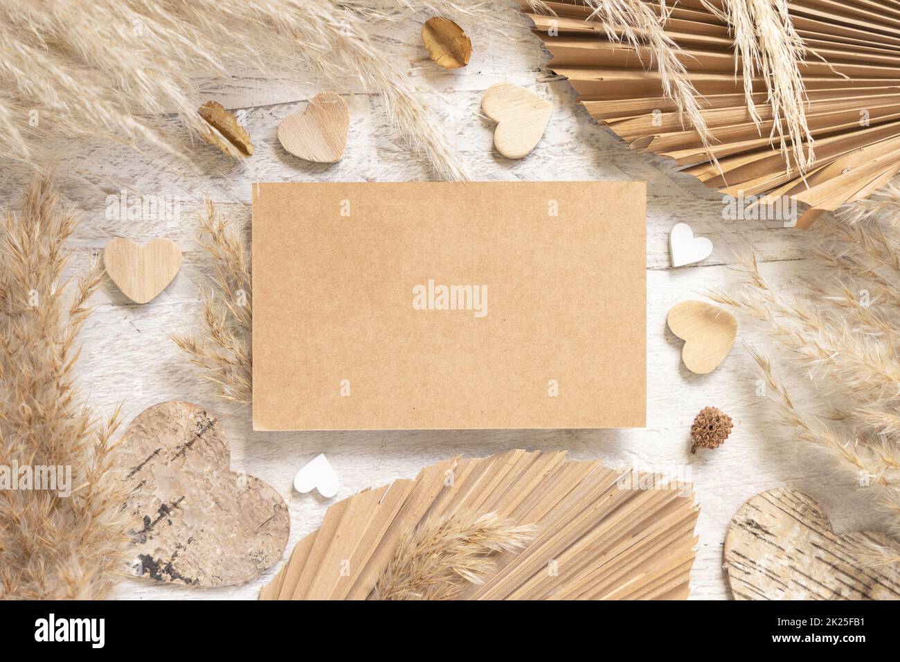 Blank card on white wooden table near dried plants, palm leaves, pampas
