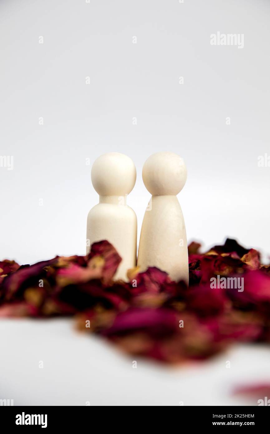 Real love, lover, couple concept. Two wooden figures with red rose petals on white background, standing together isolated on white background. copy space Stock Photo