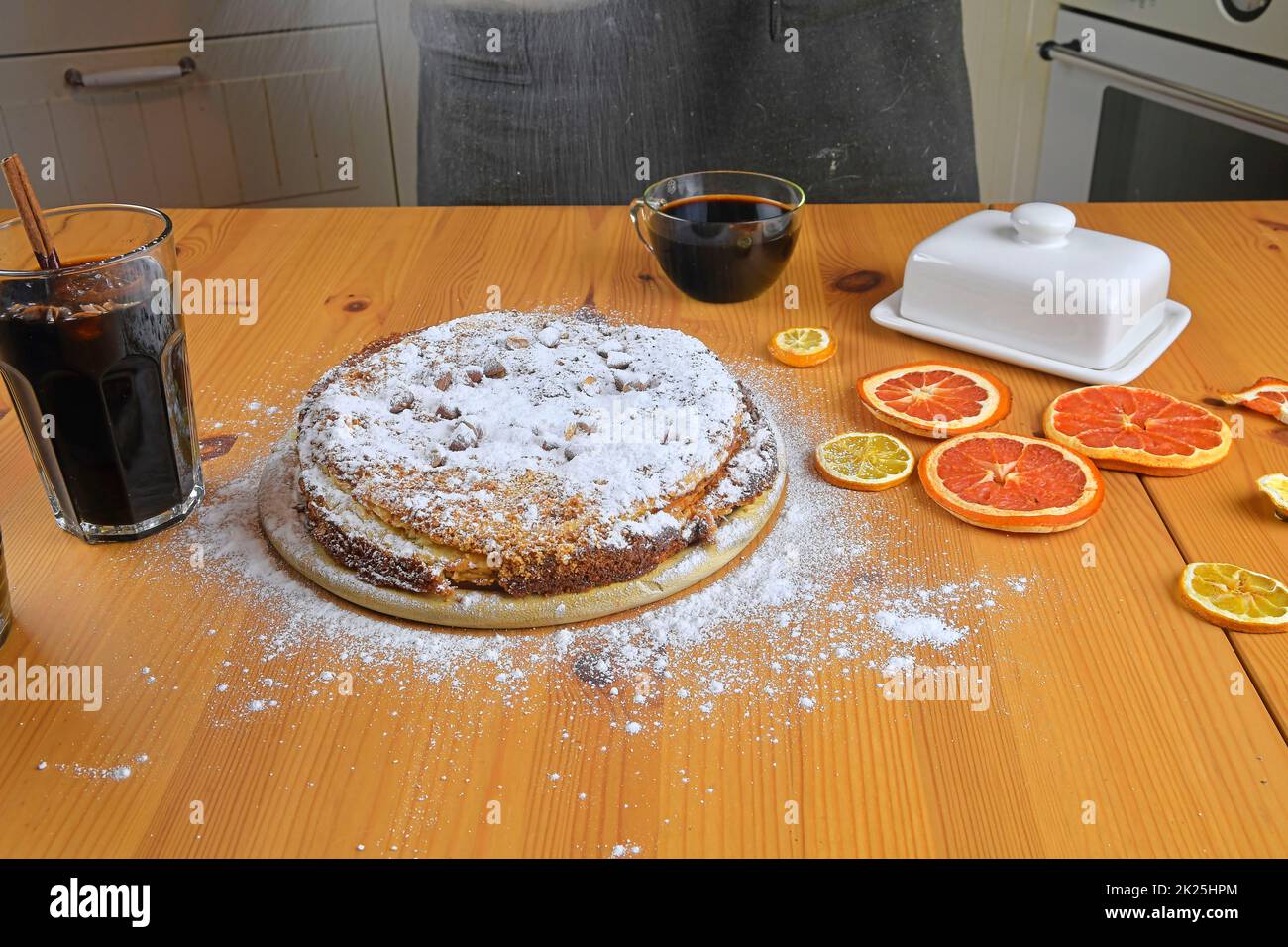 Man sprinkles powdered sugar on home-made cake. A wooden table and kitchen background Stock Photo