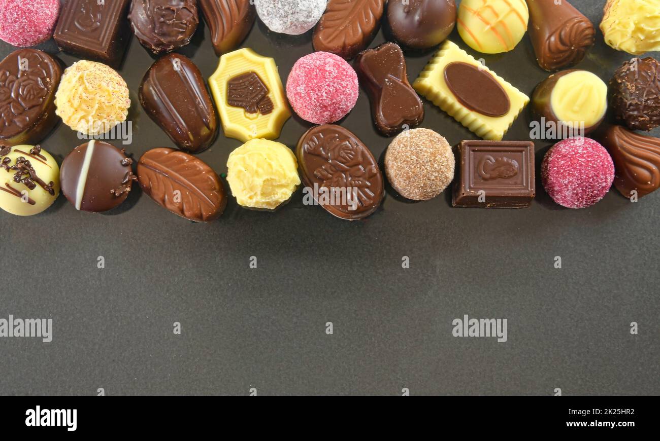 Chocolate pralines frame top view stock images. Chocolate candies on a black background. Chocolate frame top view. Chocolate pralines background with copy space for text. Border of different candies Stock Photo