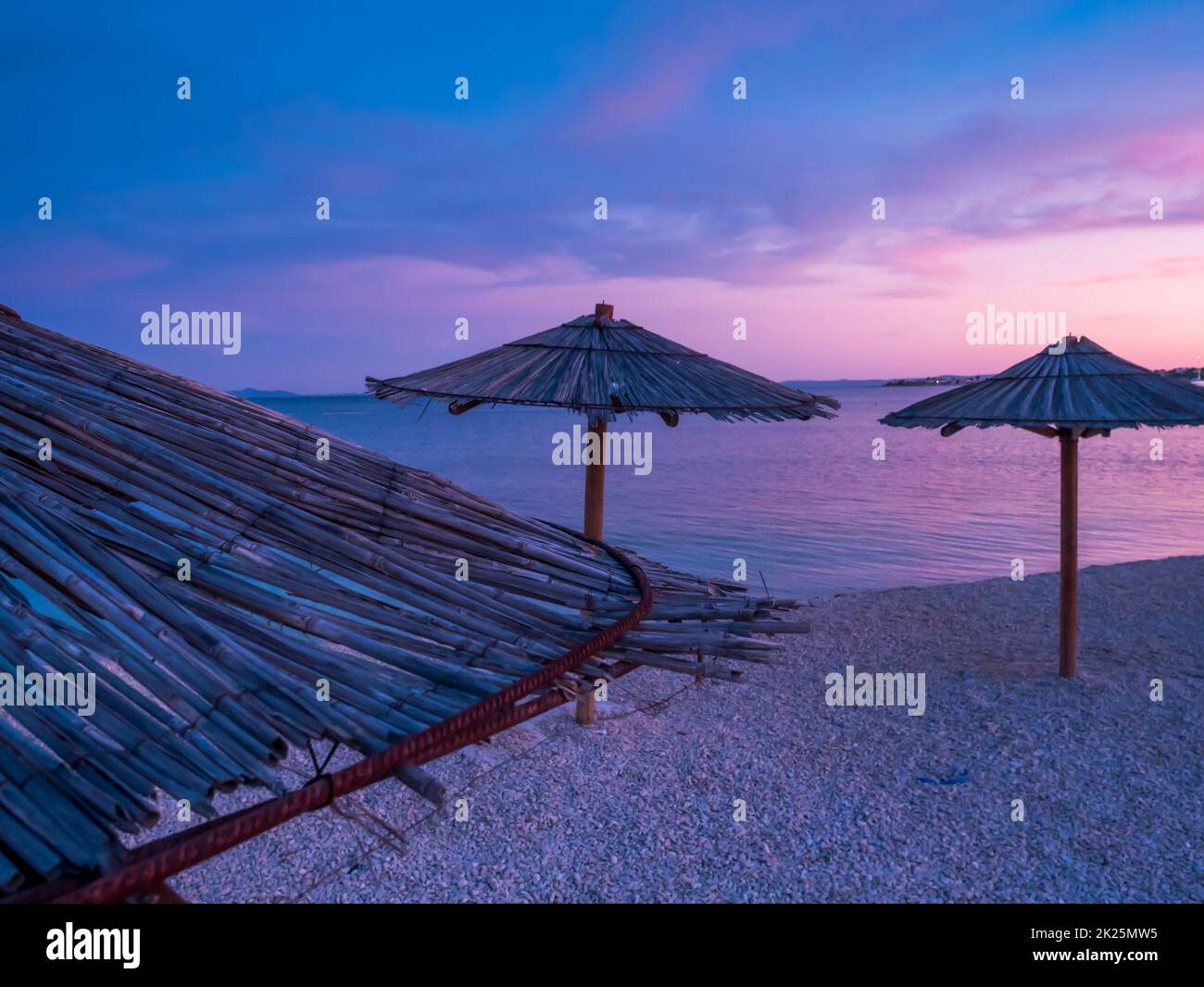 View of the beautiful blue and purple sunset, sky and straw beach umbrellas Stock Photo