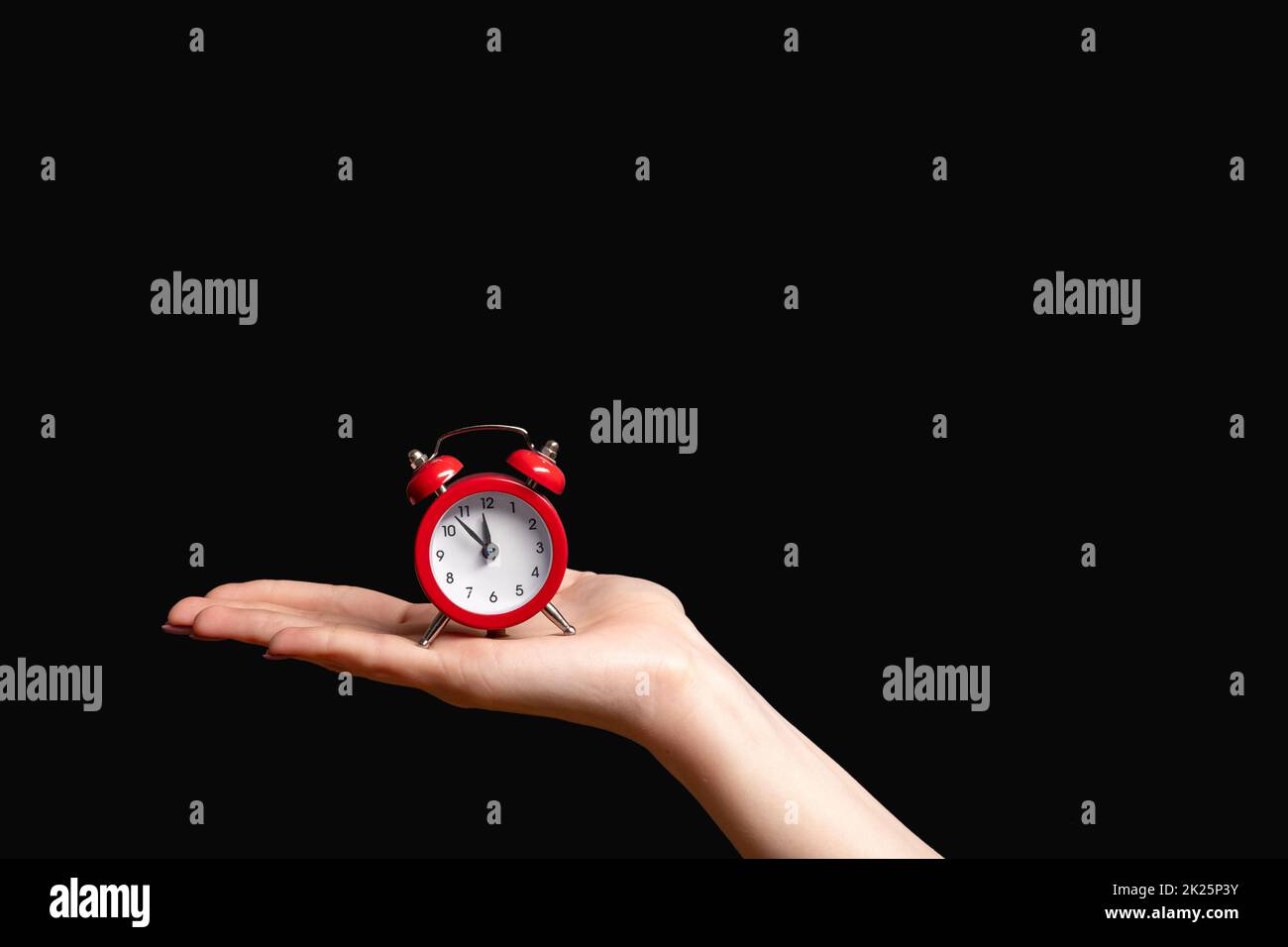 Time management. Deadline reminder. Hurry up. Female hand holding vintage miniature red alarm clock on open palm isolated on black copy space backgrou Stock Photo
