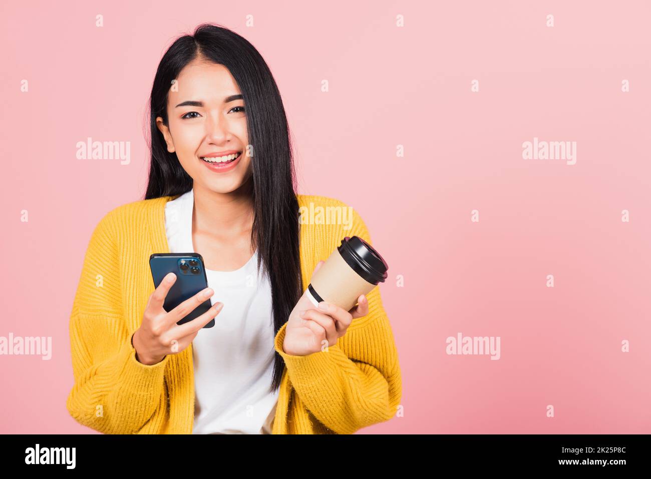 Happy Asian portrait beautiful cute young woman excited smiling holding mobile phone and coffee to go, studio shot isolated on pink background, female using smartphone with coffee cup take away Stock Photo