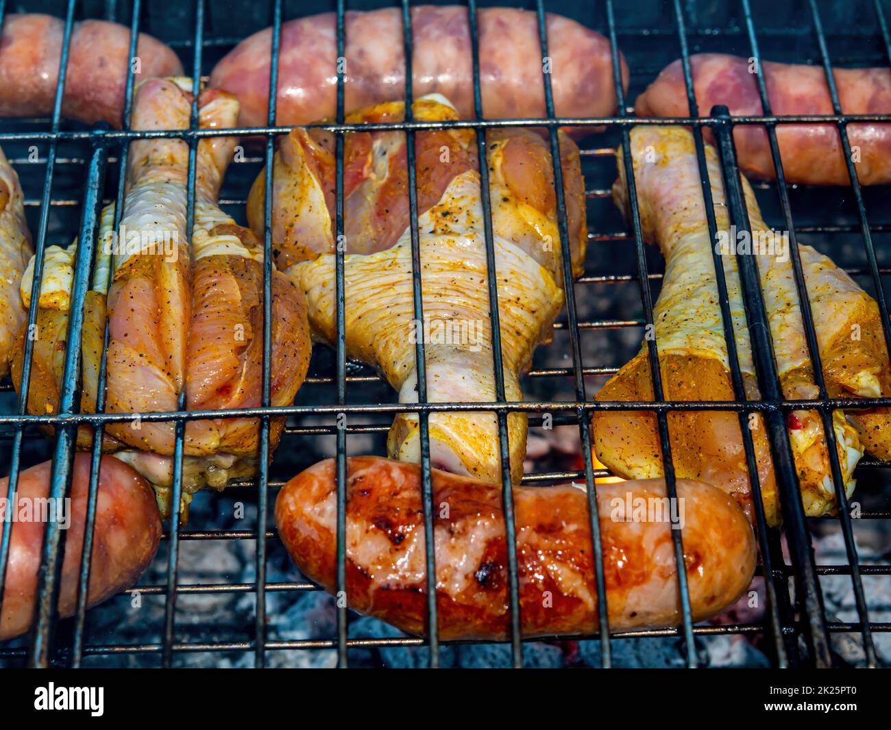 Chicken legs and meat sausages on an iron grill mesh. Stock Photo