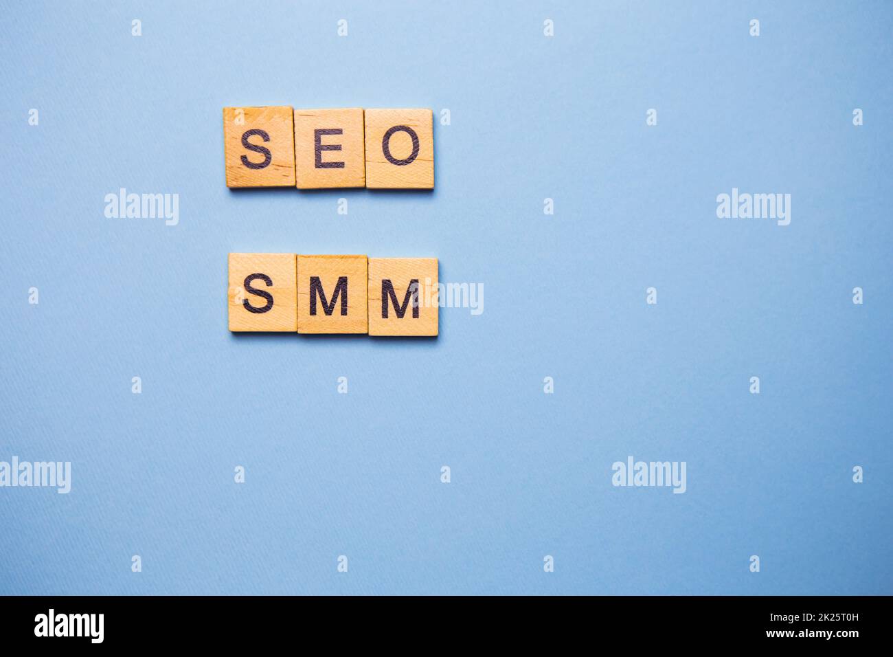Wooden letters SEO and SMM are printed on a light blue background. Stock Photo