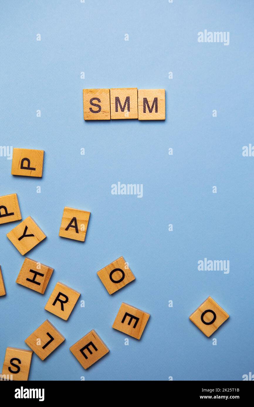 Wooden letters SMM are printed on a light blue background with many different wooden letters on the background. Stock Photo