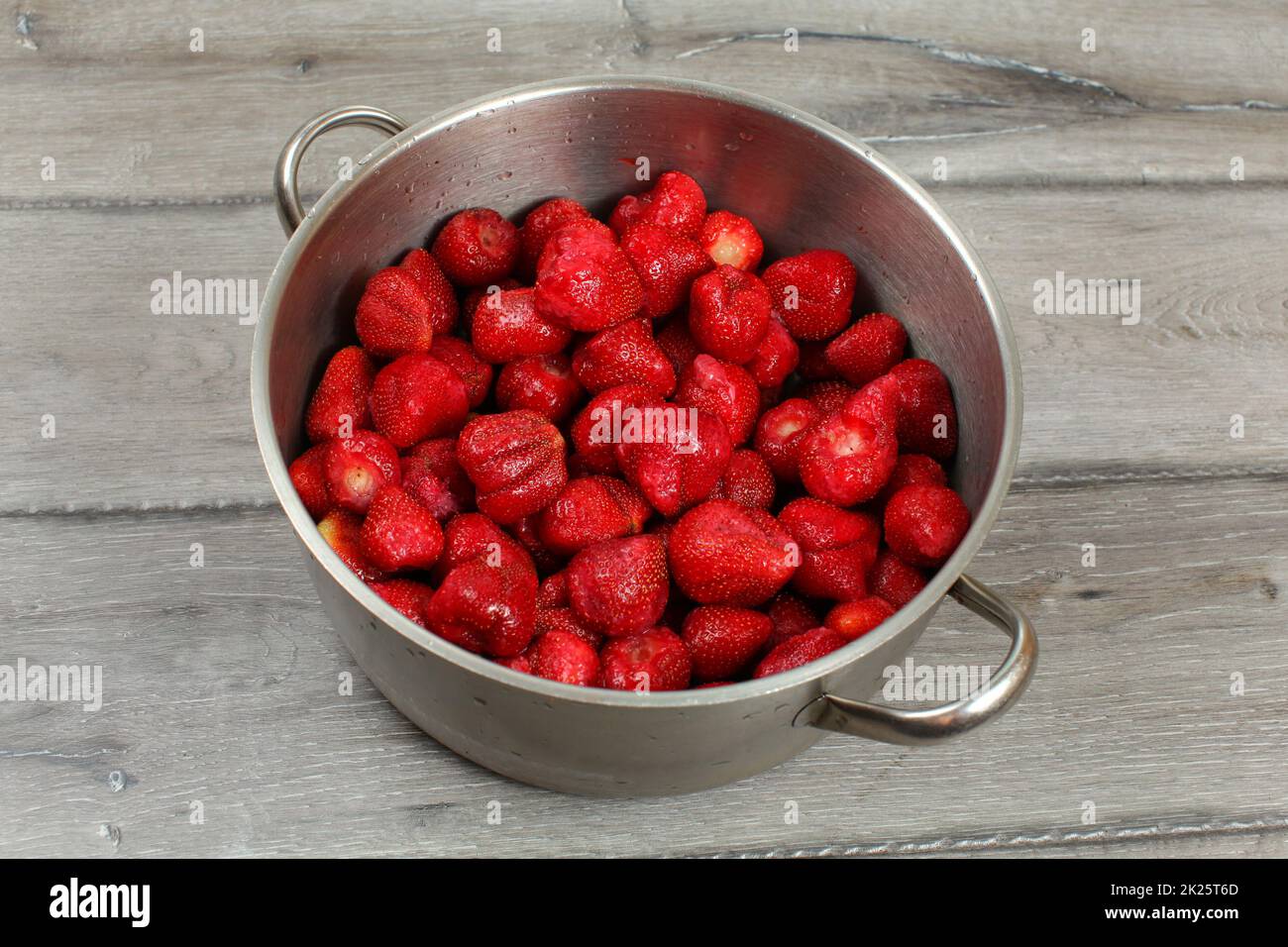 Stainless steel cooking pot full of strawberries on wooden desk. Homemade strawberry jam preparation. Stock Photo