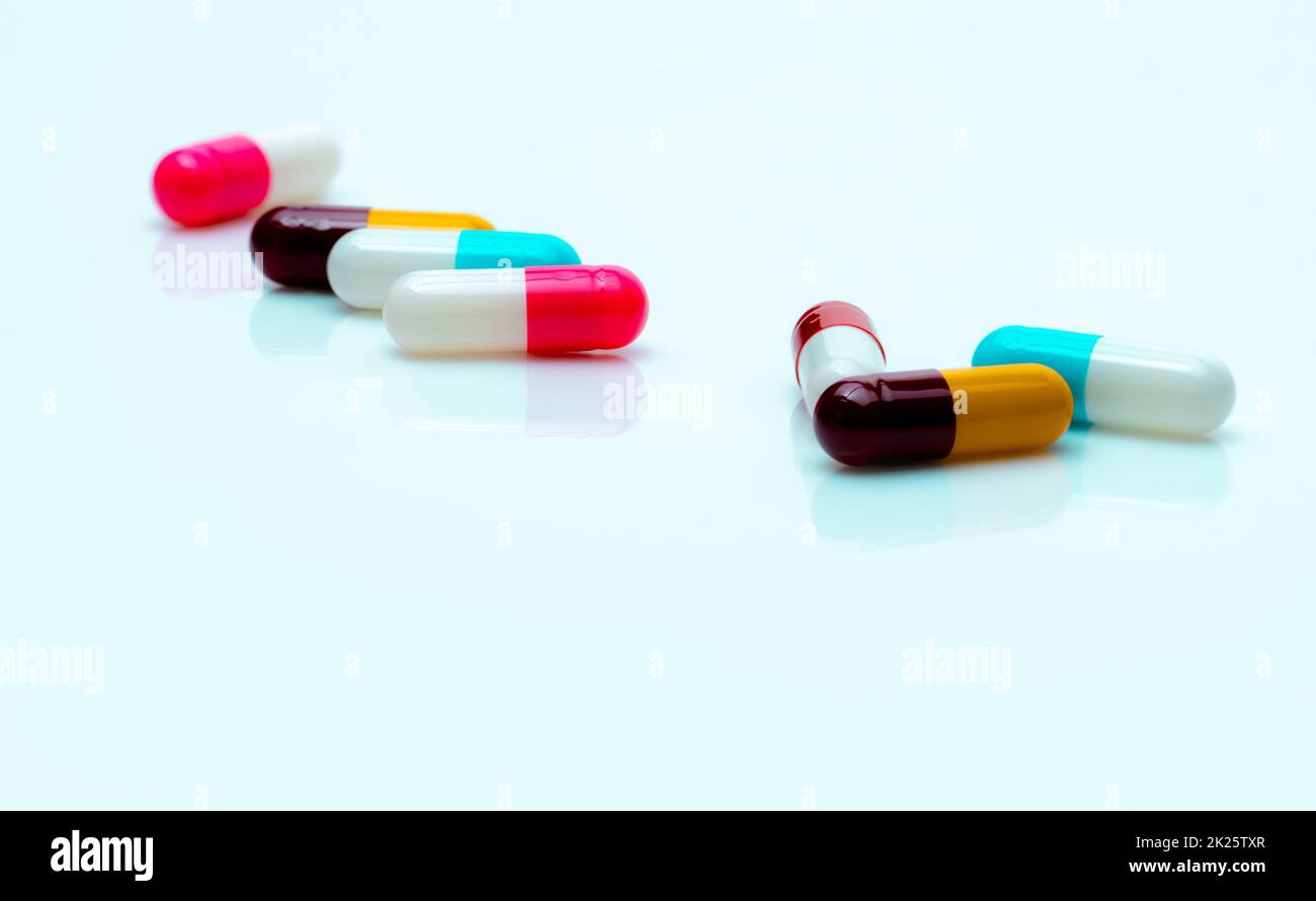 Multi-color antibiotic capsule pills spread on white background. Antibiotic drug resistance. Antimicrobial capsule pills. Pharmaceutical industry. Pink, white, blue, yellow, and red capsule pills. Stock Photo
