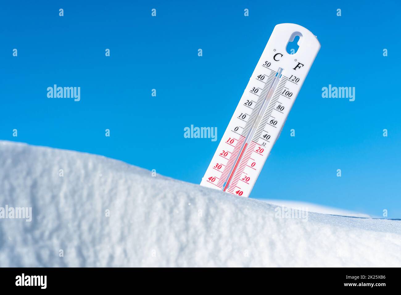 The thermometer lies on the snow and shows a negative temperature in cold weather on the blue sky.Meteorological conditions with low air and ambient temperatures.Climate change and global warming Stock Photo