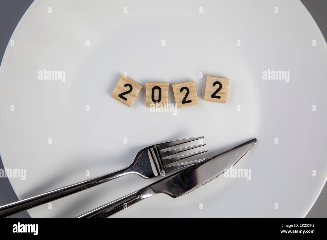 Fork and knife on a white empty plate with 2022 text top view, New year