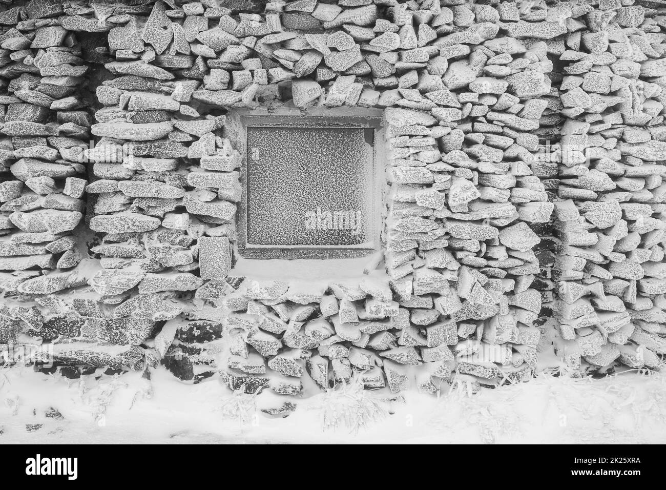 Stone wall and windows of an old and abandoned building covered with ice and snow. Background. Black and white. Stock Photo