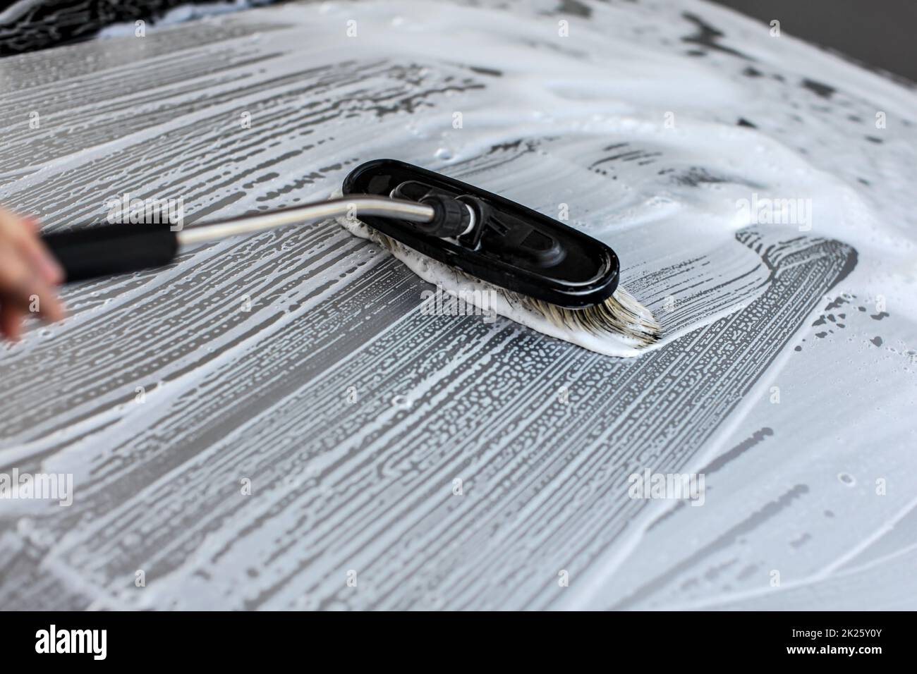 Brush leaving strokes in white shampoo and foam on roof of silver car washed in self serve