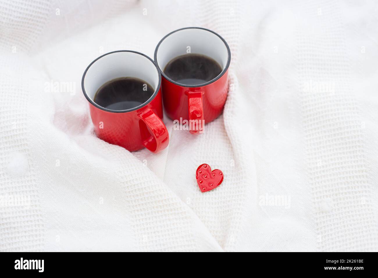 Two red cups of coffee together with a small red heart, coffee in bed. Surprise, valentine's day celebration concept. Stock Photo