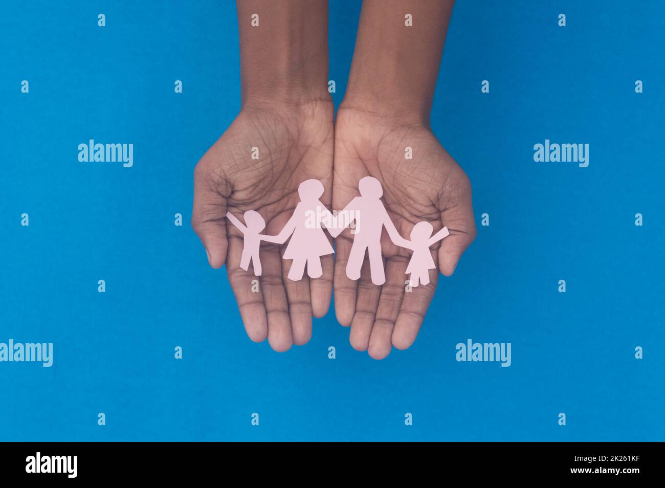 Hand holding family figure cutout top view. World health day Protection against domestic violence, healthcare and medical background. Foster care, homeless support and social distancing concept. Stock Photo