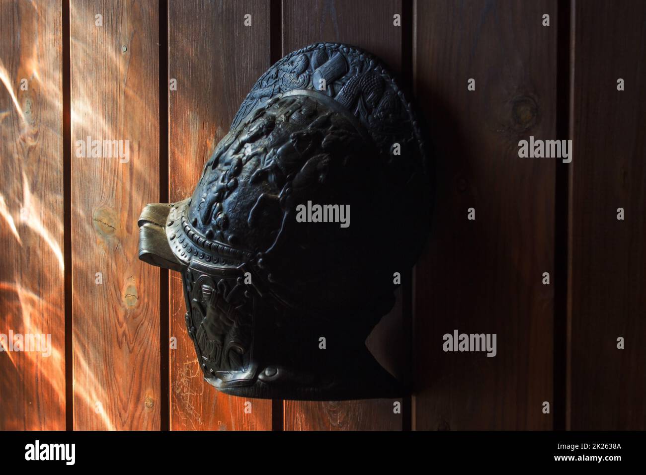 Ancient metal helmet hung on wood paneling Stock Photo