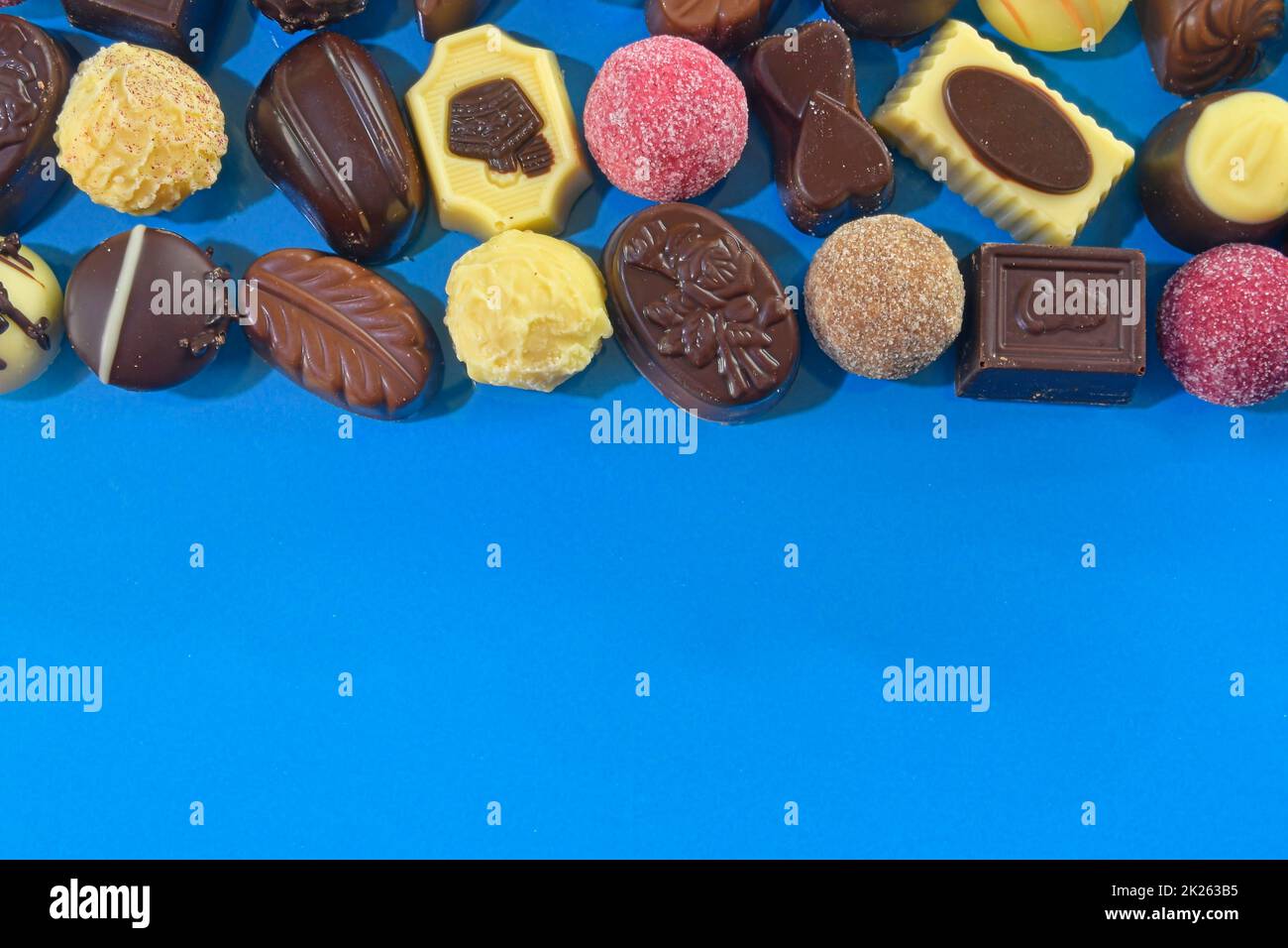 Chocolate pralines frame top view stock images. Chocolate candies on a blue background. Chocolate frame top view. Chocolate pralines background with copy space for text. Border of different candies Stock Photo