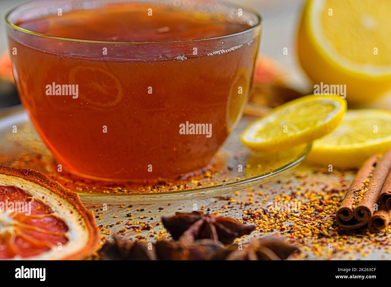 Cup with hot tea and steam on black. Glass cup of black tea with cinnamon sticks, anise star, lemon and dried fruit on white wooden table background. Macro image Stock Photo