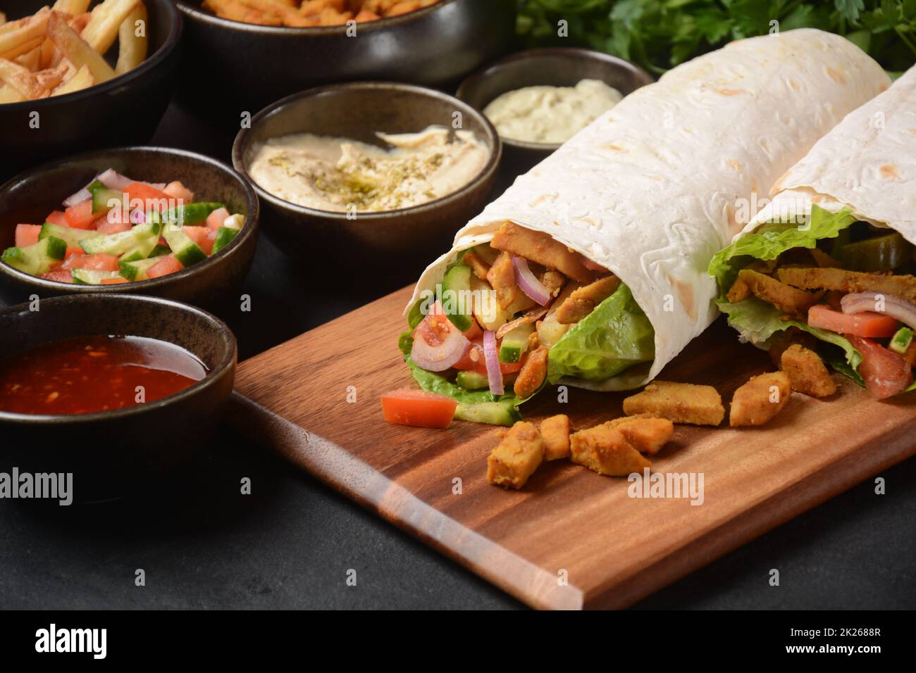 Shawarma Rolled Sandwich with Sauce and vegetables, Arab Traditional Food. Shawarma Doner kebab wrap with chicken, fries and pickles. Israeli Traditional homemade Shawarma on wooden cutting board. Stock Photo