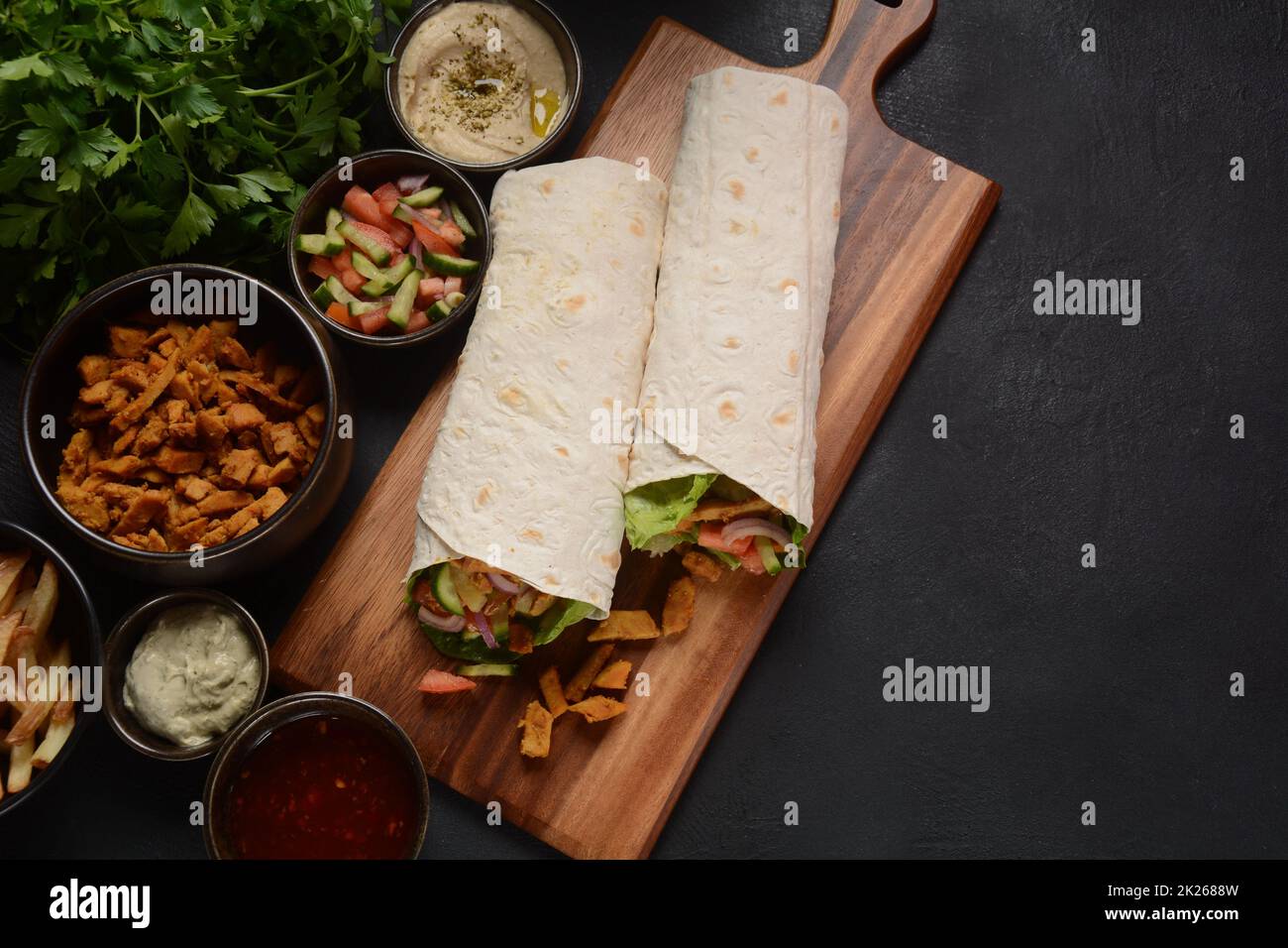 Shawarma Rolled Sandwich with Sauce and vegetables, Arab Traditional Food. Shawarma Doner kebab wrap with chicken, fries and pickles. Israeli Traditional homemade Shawarma on wooden cutting board. Stock Photo
