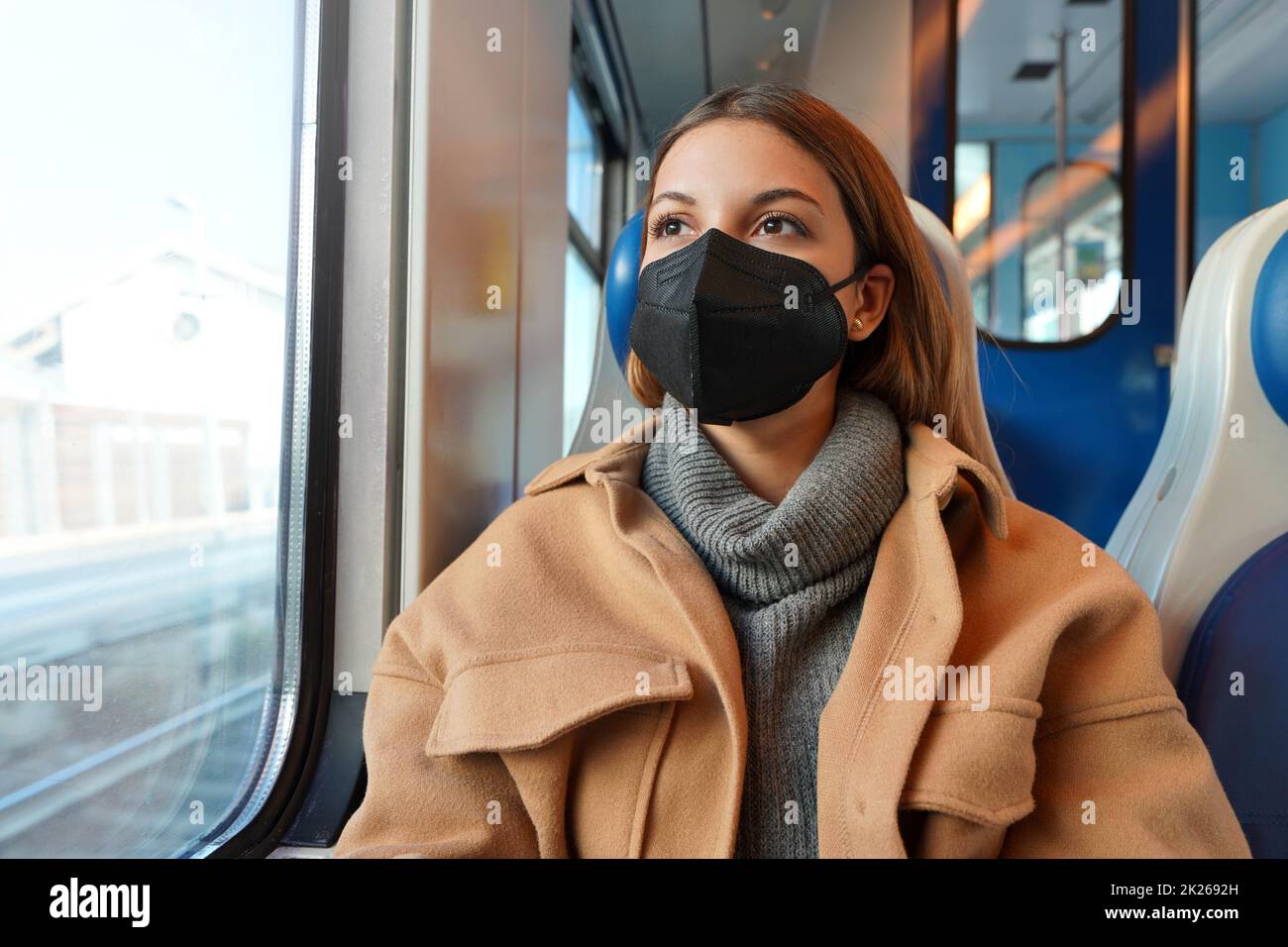 Young thoughtful woman wearing black medical face mask on train looking