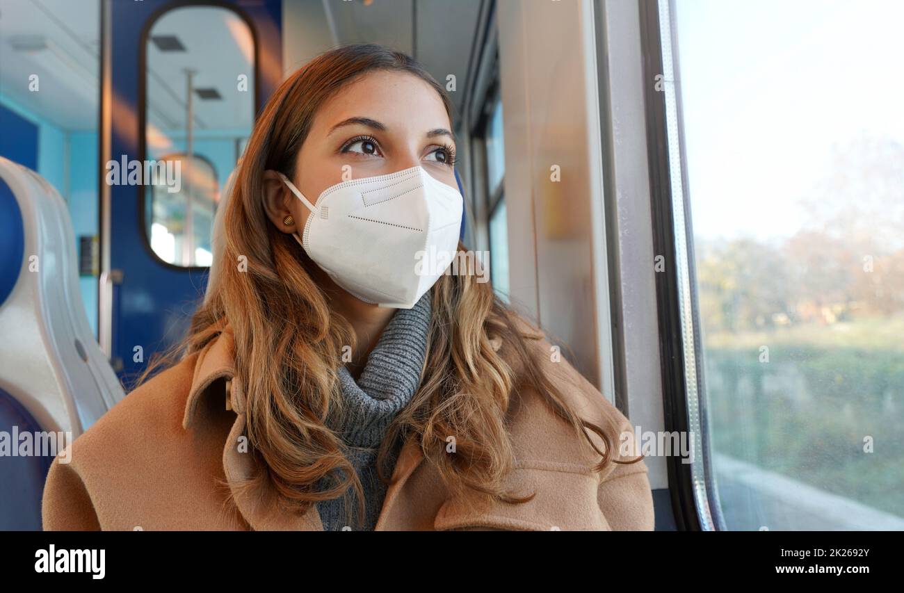 Travel safely on public transport. Panoramic banner of beautiful woman wearing FFP2 KN95 face mask on train looking through the window. Stock Photo