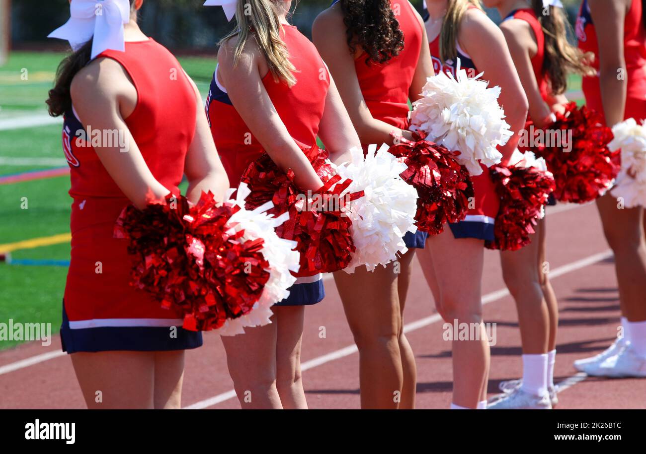 Rear view of cheerleaders on the sideline with their pom poms during a football game. Stock Photo
