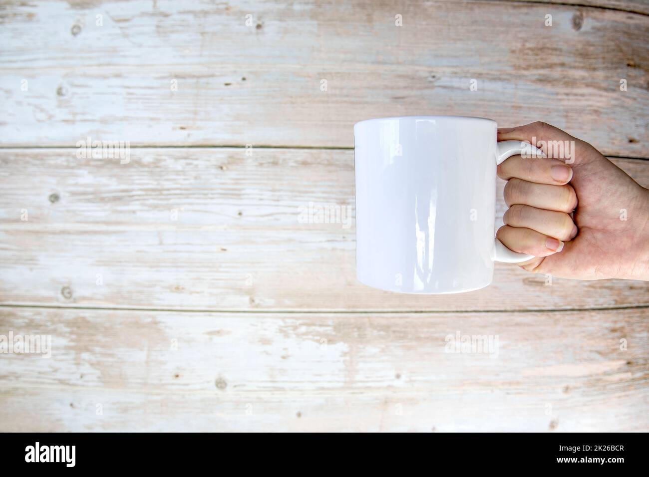 Hand holding a ceramic mug blank on wooden background with copy space Stock Photo