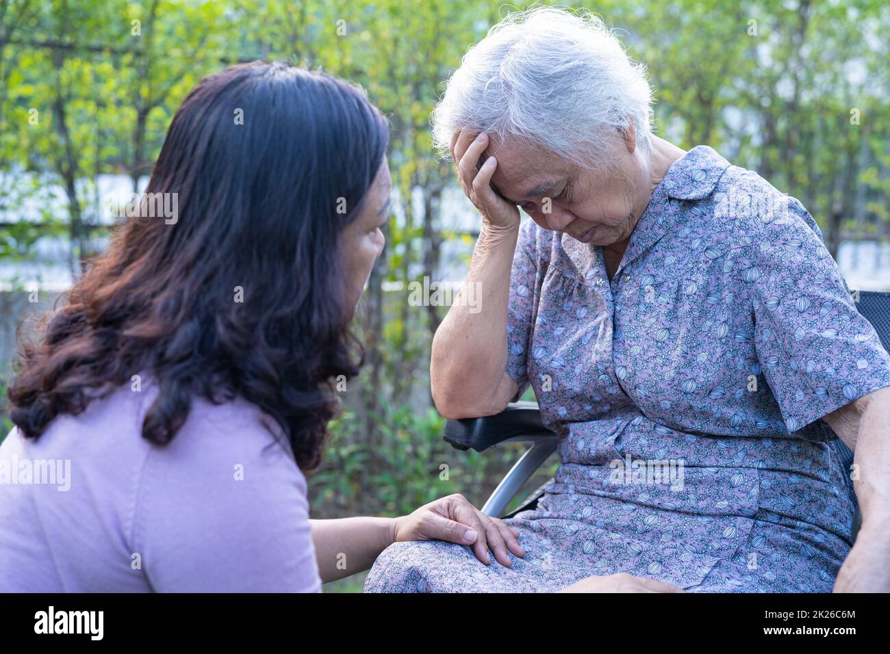 Caregiver help Asian senior or elderly old lady woman patient headache while sitting on wheelchair in park. Stock Photo
