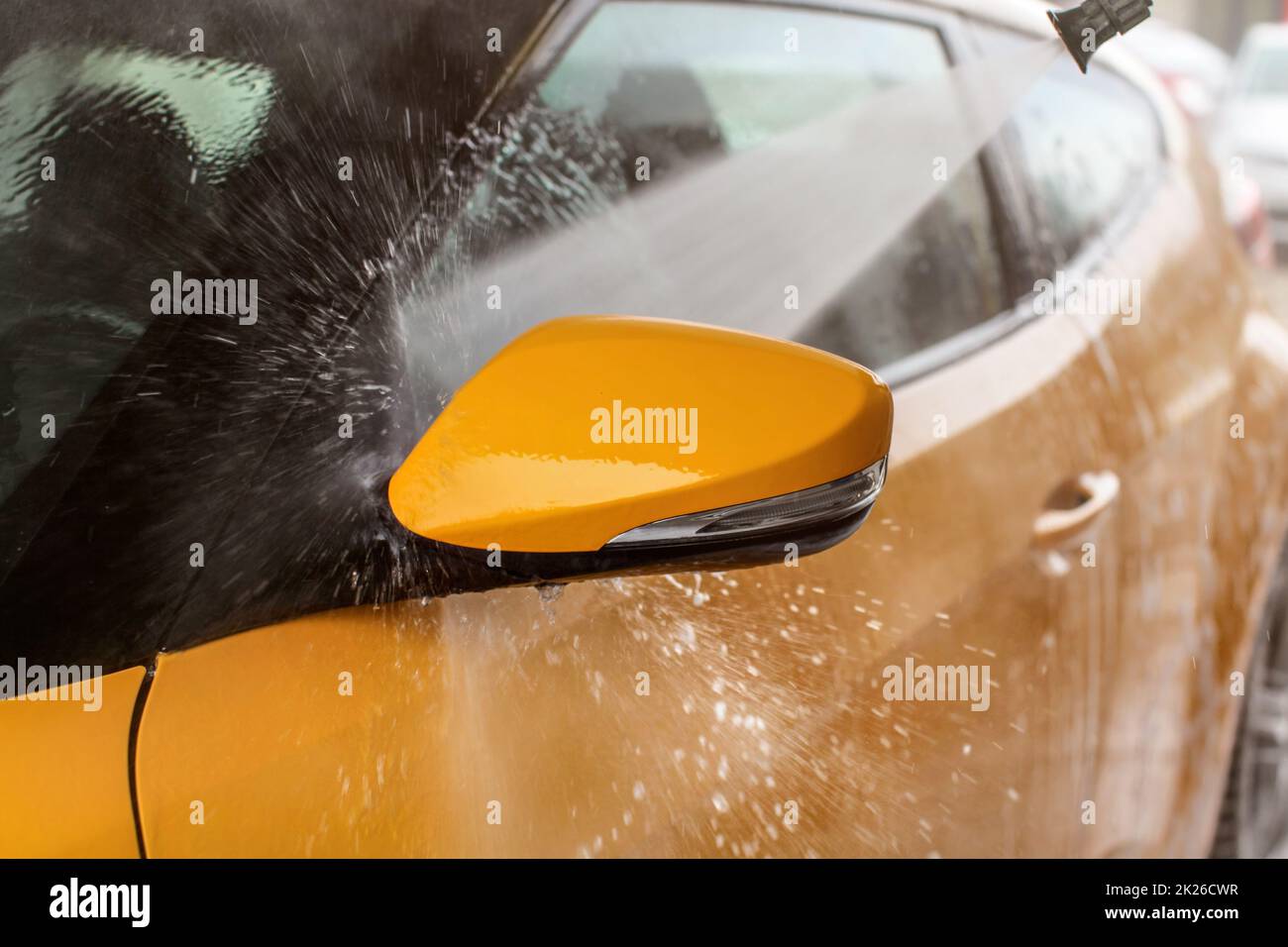Side mirror of yellow car washed in self service carwash, jet spray of